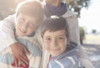 Two young sons stand in front of their mother who has her arm wrapped around them